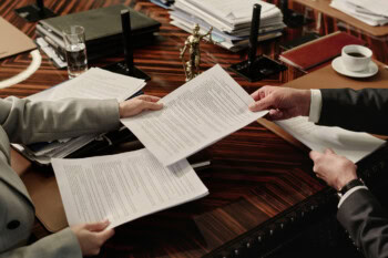 Two Attorneys Exchanging Documents Sitting Side by Side at Table